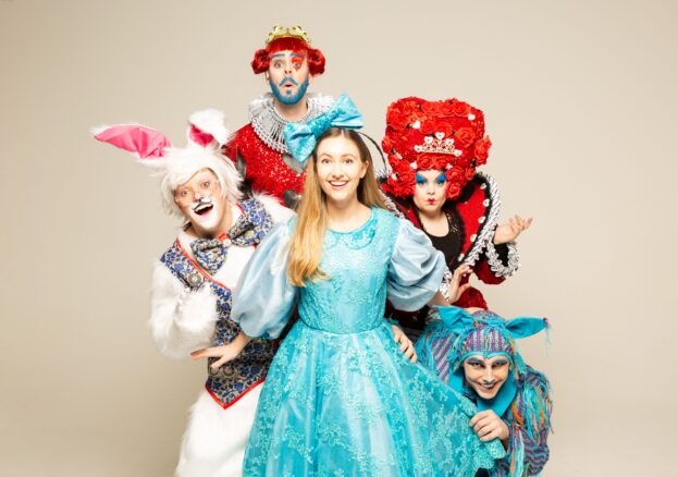 Alice in Wonderland at Waterside Arts. Alice is shown in a blue dress characters from the story behind her including the white rabbit and the Queen of Hearts. Part of our half term in Manchester activities