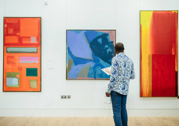 A visitor viewing three brightly coloured abstract artworks in The Stanley & Audrey Burton Gallery.