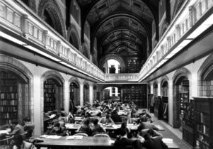 Black and white image of a traditional library setting with customers studying at desks.
