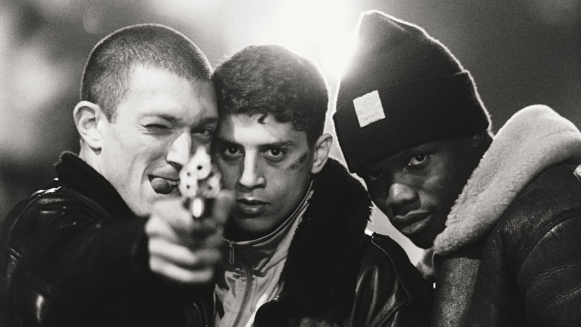 A black and white shot of three young men, holding a gun towards the camera