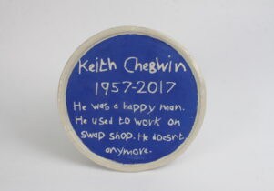 A ceramic blue plaque which says, 'Keith Chegwin 1957 - 2017. He was a happy man. He used to work on swapshop. He doesn't anymore.'