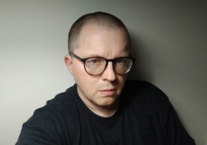 Portrait of James Womack in a black tshirt with  bald head and black rimmed glasses