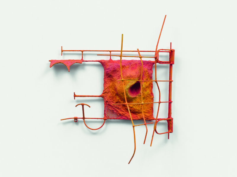 A ombre, orange, red and yellow metal sculpture hanging on a wall.