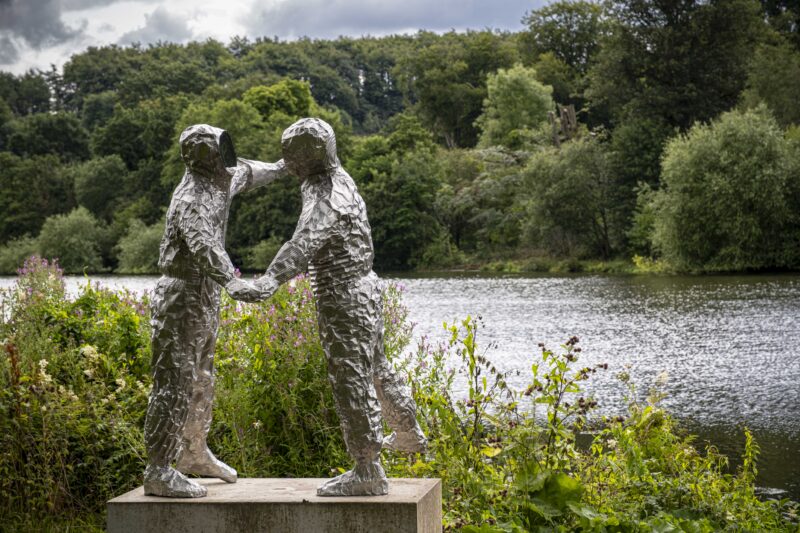 Sculpture of two figure dancing by a lake