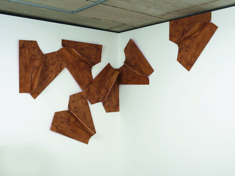 Wooden hanging sculpture in a corner of a gallery wall.