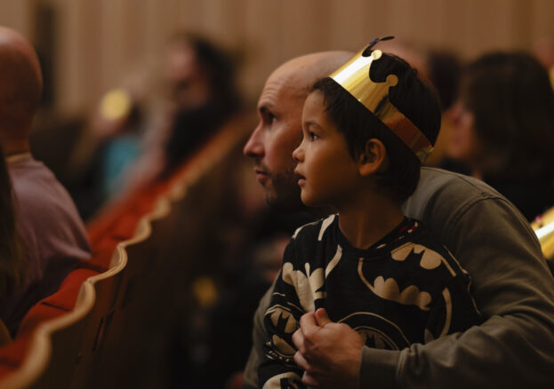 A boy wearing a paper crown watching a show in the stoller hall