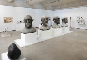 Sculptures of heads in a gallery space with works hanging on the wall