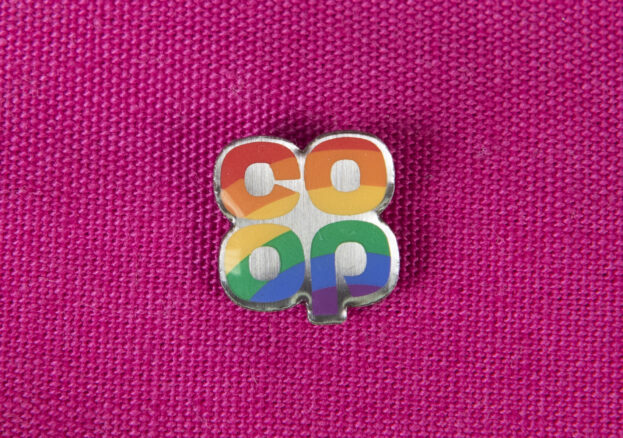 A small rainbow pin badge on a pink background. The text reads co op