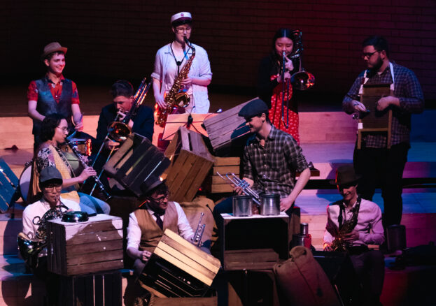 Wind musicians dressed in sailor costumes and performing on wooden crates