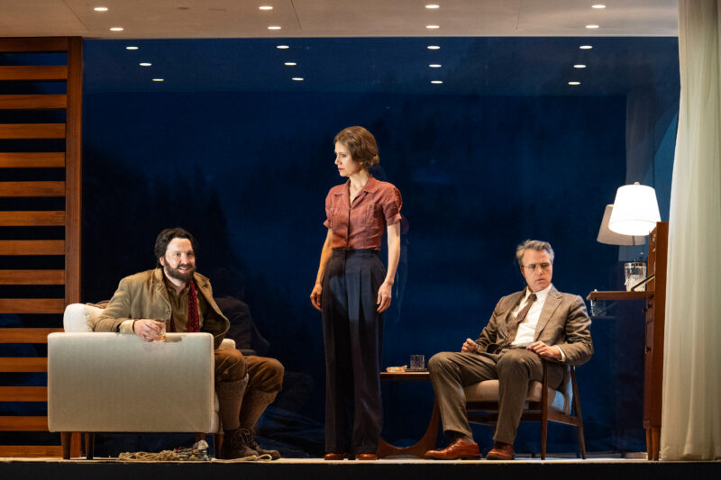 Blond Eckbert production image. Two men sat in armchairs with woman stood in between them.