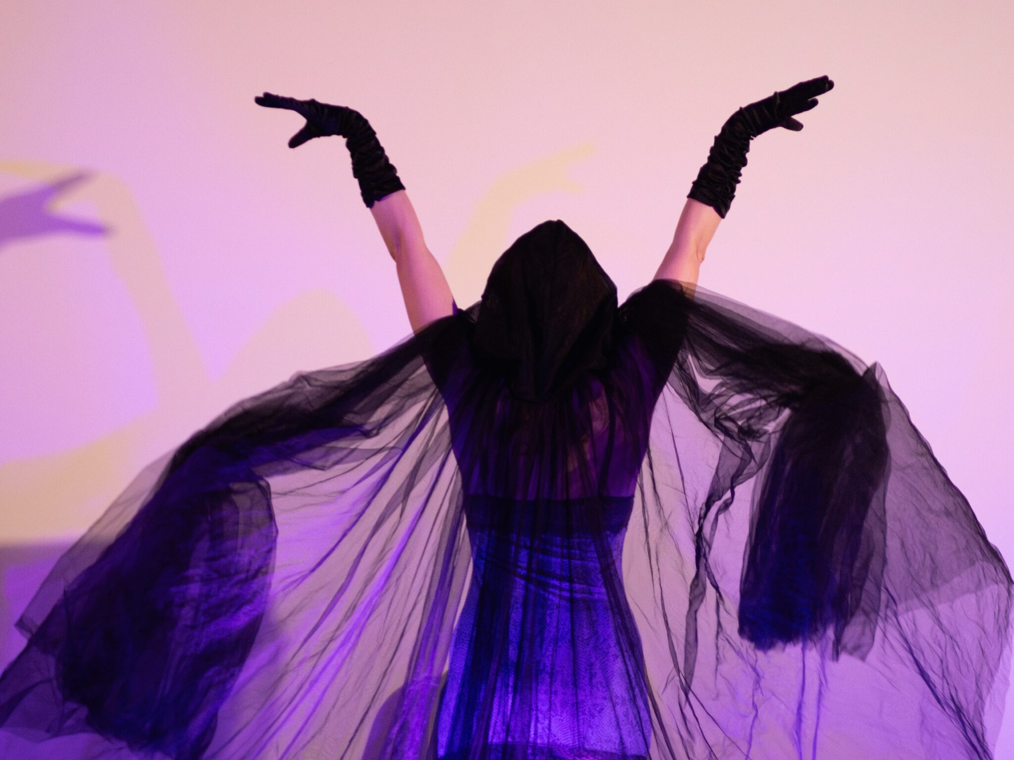 Ember Travixen, a burlesque performer, onstage wearing a black hooded cloak that is billowing around her