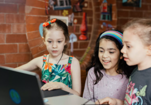 Three children look at a laptop screen.