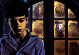 Boy in front of a window where there is a ghostly looking boy looking through it.