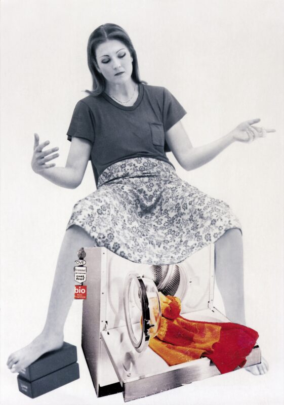 A photograph of a woman sitting on a washing machine. The washing machine door is open and red, orange and yellow towels is draped out of the washing machine door.  