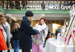 A smiling market trader shows a customer a painting in Victoria Baths