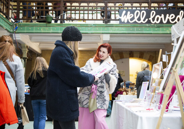 A smiling market trader shows a customer a painting in Victoria Baths