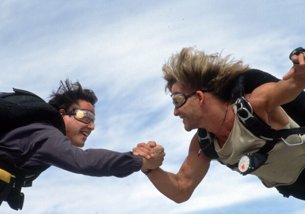 Point Break. Two men embracing as they parachute.