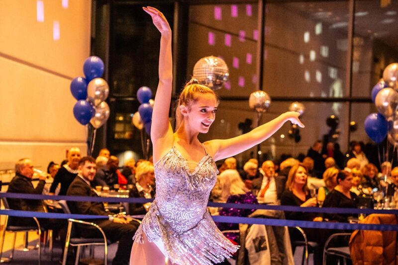 A woman in a silver dress dancing in front of a seated audience