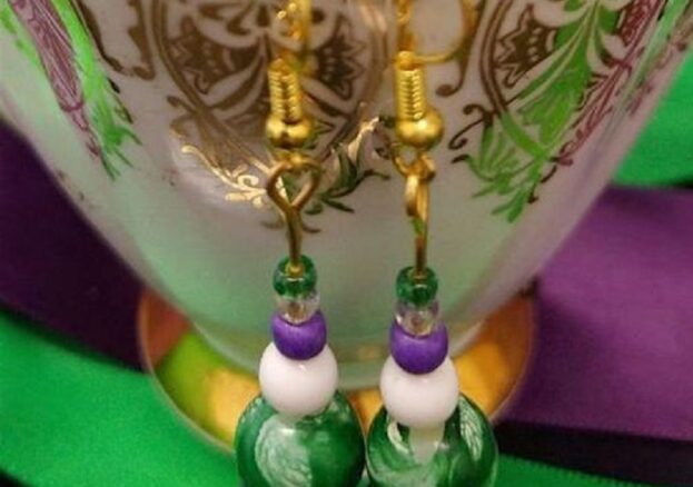 A pair of purple, white and green earrings hanging on the rim of a china teacup