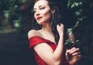 Woman with long brown hair in red dress surrounded by trees