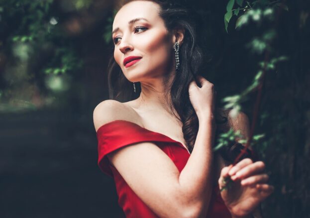 Woman with long brown hair in red dress surrounded by trees