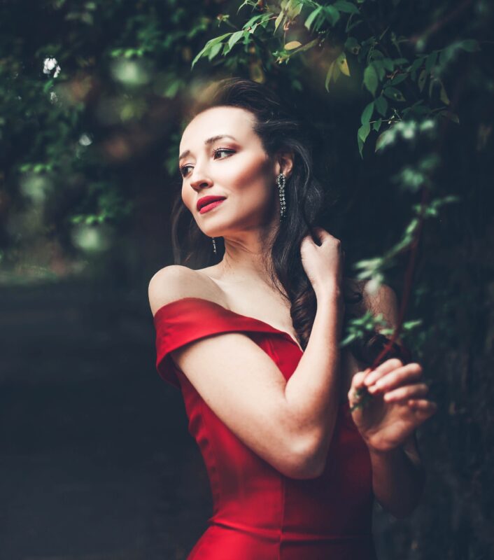 Woman with long brown hair in red dress surrounded by trees