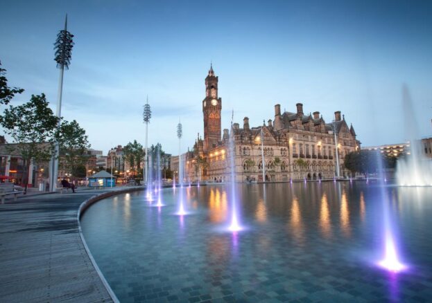 An image of a large man made pool with fountains in front of a historic building with a clock tower