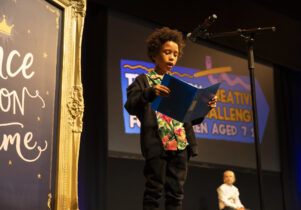 Creative writing challenge prize giving, a young boy on stage reading in front of a microphone